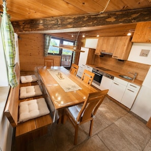 Ein Holzinterieur mit Esstisch, Stühlen, Küchenzeile und Fenster.