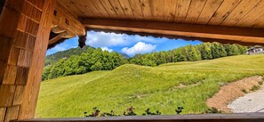 A wooden structure with a view of a green hillside and a house in the distance. - Göll Vacation Rental - 65 square meters - 2 separate bedrooms and a balcony (Schönau am Königssee)