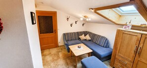 Ein kleiner, gemütlicher Raum mit einer Holztür, einem blauen Sofa, einem kleinen Tisch und einem Holzschrank.