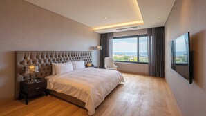 A modern hotel room with a large bed, a nightstand, a chair, a TV, and a window with a city view. - O'REVE Resort (Seogwipo)