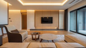 A modern living room with a sofa set, a coffee table, a flat-screen TV mounted on the wall, and a large window. - O'REVE Resort (Seogwipo)