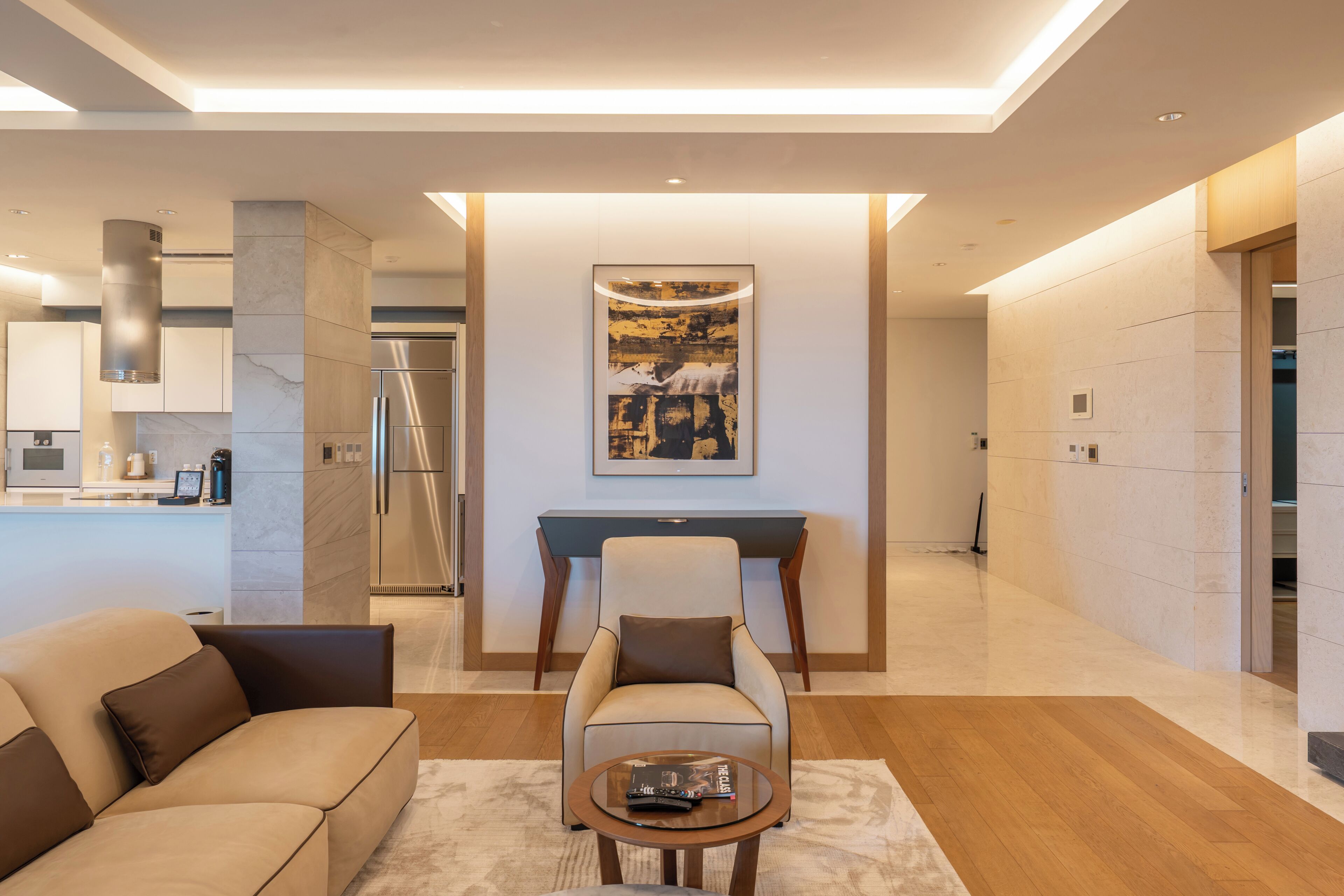 A modern living room with a sofa, armchair, coffee table, and a painting on the wall.