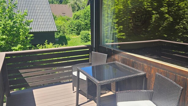 Una terraza al aire libre techada con mobiliario de mimbre y una mesa de vidrio.