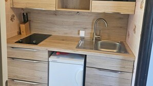 Una cocina compacta con armarios de madera, un lavamanos integrado y un refrigerador pequeño.