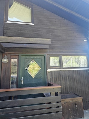 Una cabana de fusta amb una porta verda, un petit porxo i una finestra.
