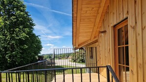 Un edifici de fusta amb un balcó, una barana metàl·lica i una vista despejada d'un paisatge verd.