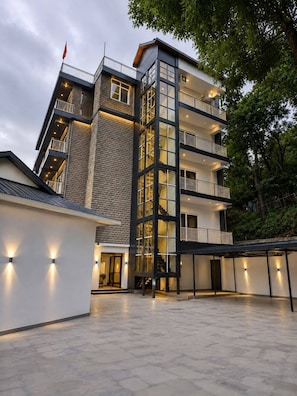 A modern multi-story building with a central staircase, balconies, and a courtyard. - Hotel Indradhar (Dharamshala)
