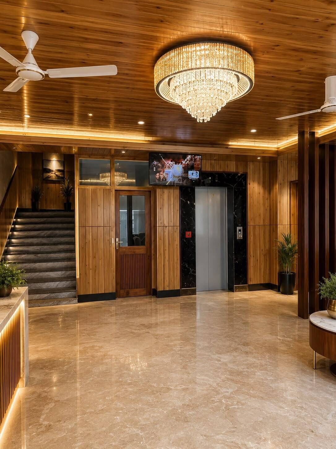 A lobby with a wooden floor, a chandelier, a ceiling fan, a staircase, and a television screen.