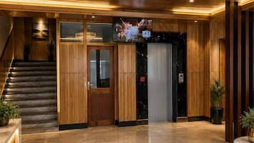A lobby with a wooden floor, a chandelier, a ceiling fan, a staircase, and a television screen.
