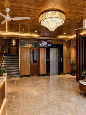 A lobby with a wooden floor, a chandelier, a ceiling fan, a staircase, and a television screen. - Hotel Indradhar (Dharamshala)