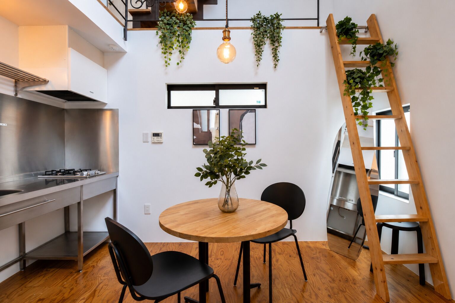 A modern kitchen with a round wooden table, black chairs, and a wooden ladder with plants.