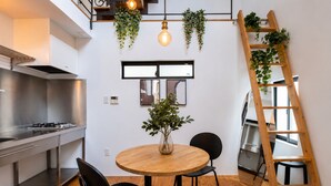 A modern kitchen with a round wooden table, black chairs, and a wooden ladder with plants. - Olive Stay Osaka (Osakashi nishiku)