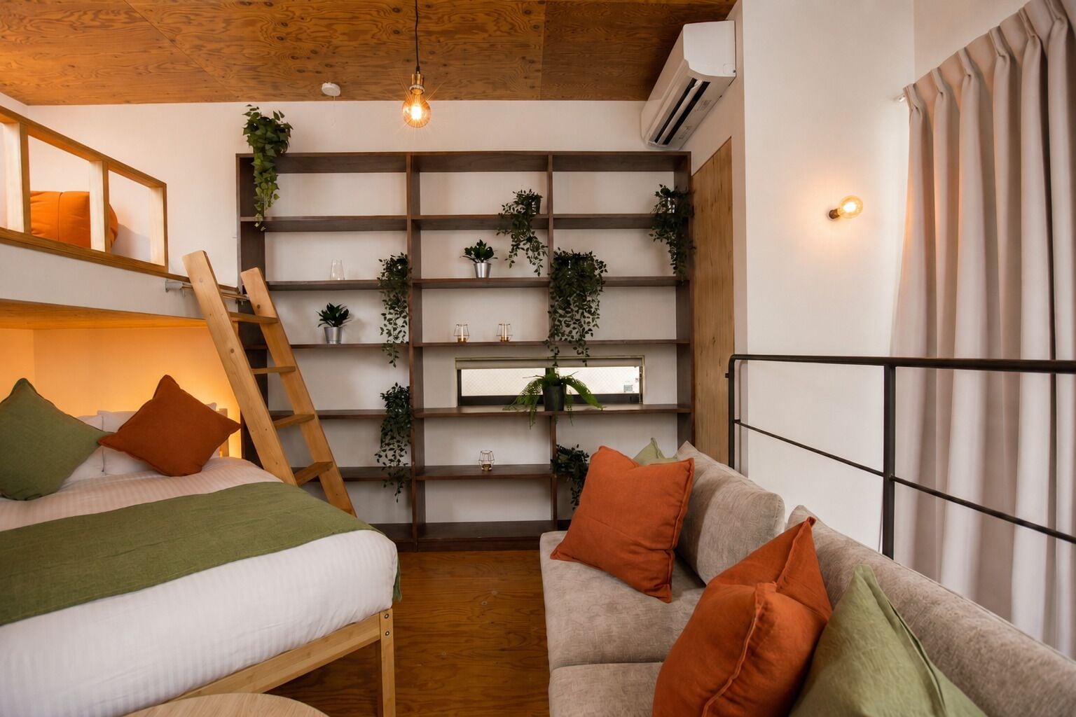 A room with a loft bed, a sofa, a ladder, shelves with plants, and a window with curtains.