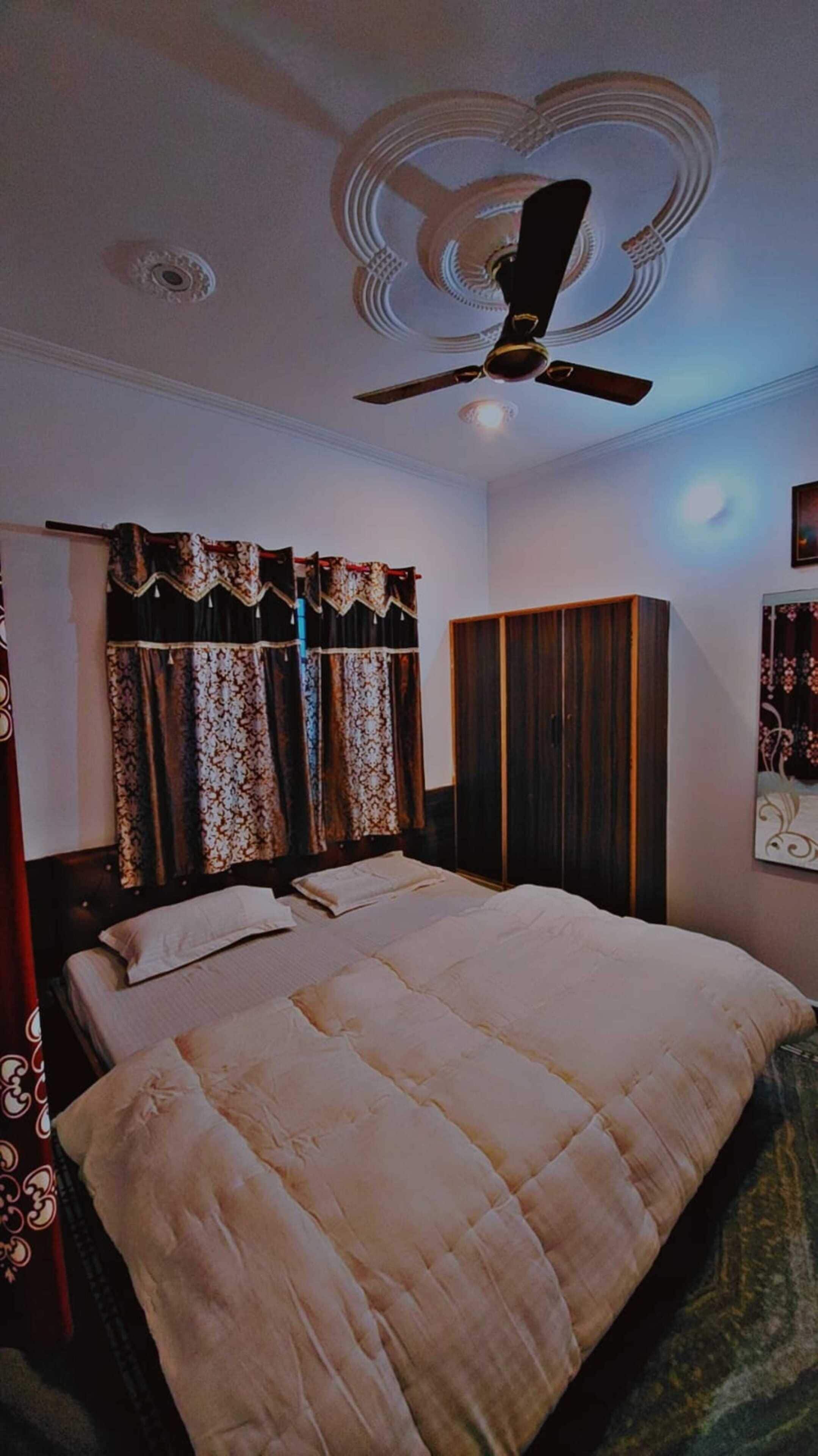 Une chambre à coucher avec un lit, des rideaux, un ventilateur de plafond et une armoire.