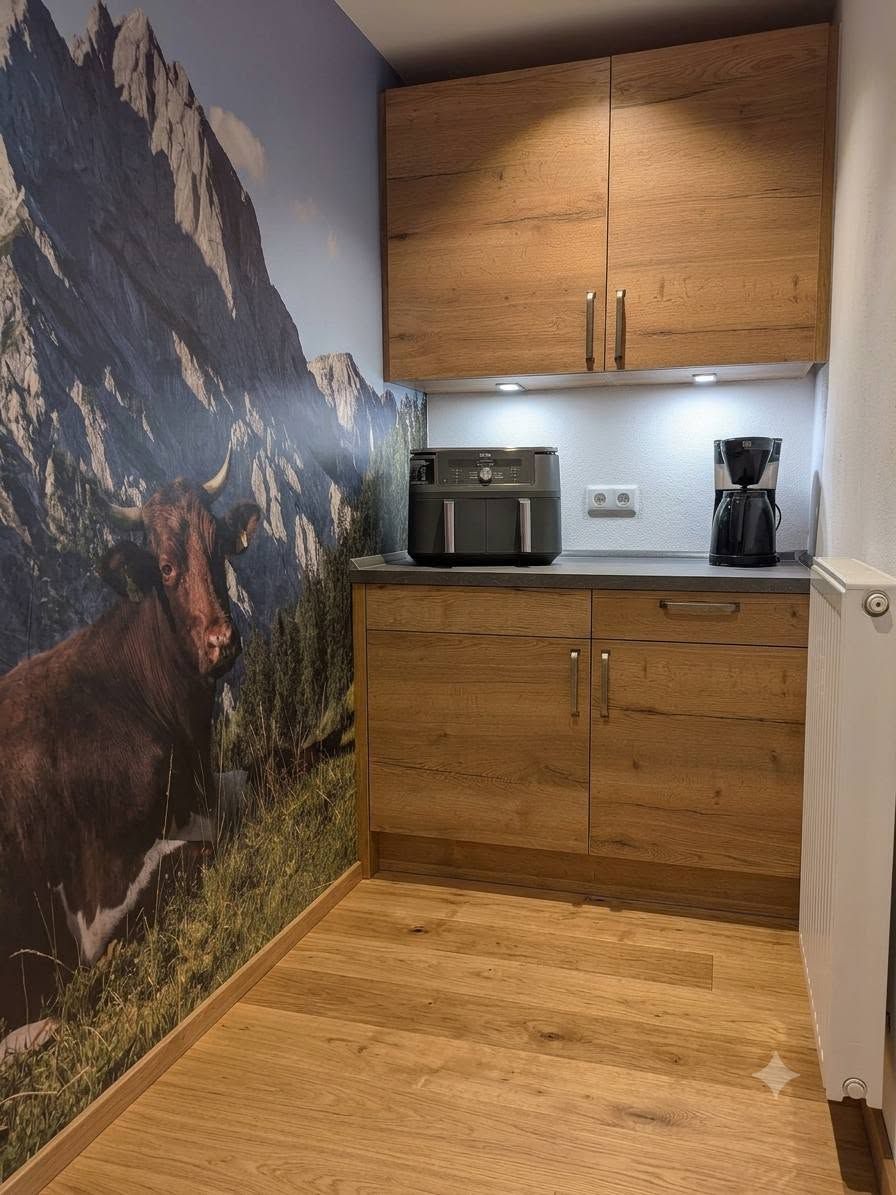 Una cocina con armarios de madera, cafetera y un mural de montañas en la pared.