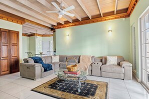 Ein Wohnzimmer mit einer Eckcouch, einem Glastisch, einem Deckenventilator und einem großen Fenster.