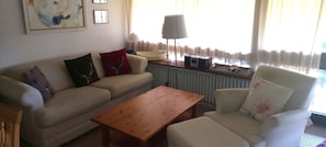 A living room with a sofa, armchair, wooden coffee table, lamp, and a radiator.
