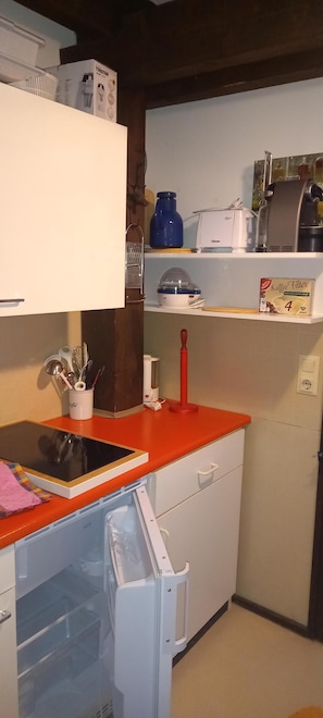 A compact kitchen with a refrigerator, a coffee maker, a toaster, and a coffee filter box.