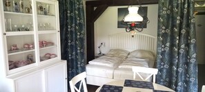 A bedroom with a bed, a bedside table, a chair, a cabinet with glass doors, and a hanging light fixture. - Iris 4 Vacation Rental (Siegsdorf)