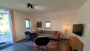 A modern living room with a sofa, chairs, a coffee table, a TV, and a lamp. - Secret van Otterlo 6 (Otterlo)