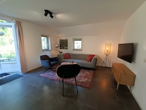 Ein modernes Wohnzimmer mit einer Couch, Sesseln, einem Couchtisch, einem Fernseher und einer Lampe.