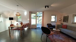 A modern living room with a dining area, a sofa, a TV, and a large window. - Secret van Otterlo 6 (Otterlo)