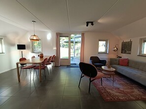 Ein modernes Wohnzimmer mit Essbereich, einer Couch, einem Fernseher und einem großen Fenster.