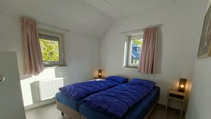 A bedroom with a bed, two bedside tables, a window, and a radiator. - Secret van Otterlo 6 (Otterlo)