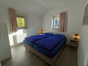 Ein Schlafzimmer mit einem Bett, zwei Nachttischen, einem Fenster und einer Heizung.