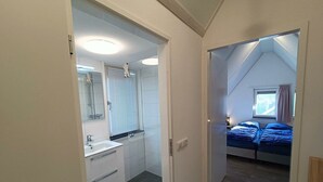 A bedroom with a window, a bed, and a bathroom with a sink and mirror. - Secret van Otterlo 6 (Otterlo)