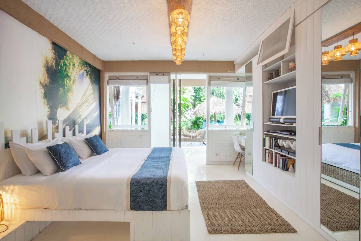 Un dormitorio con cama, una estantería, un televisor y un ventanal grande.