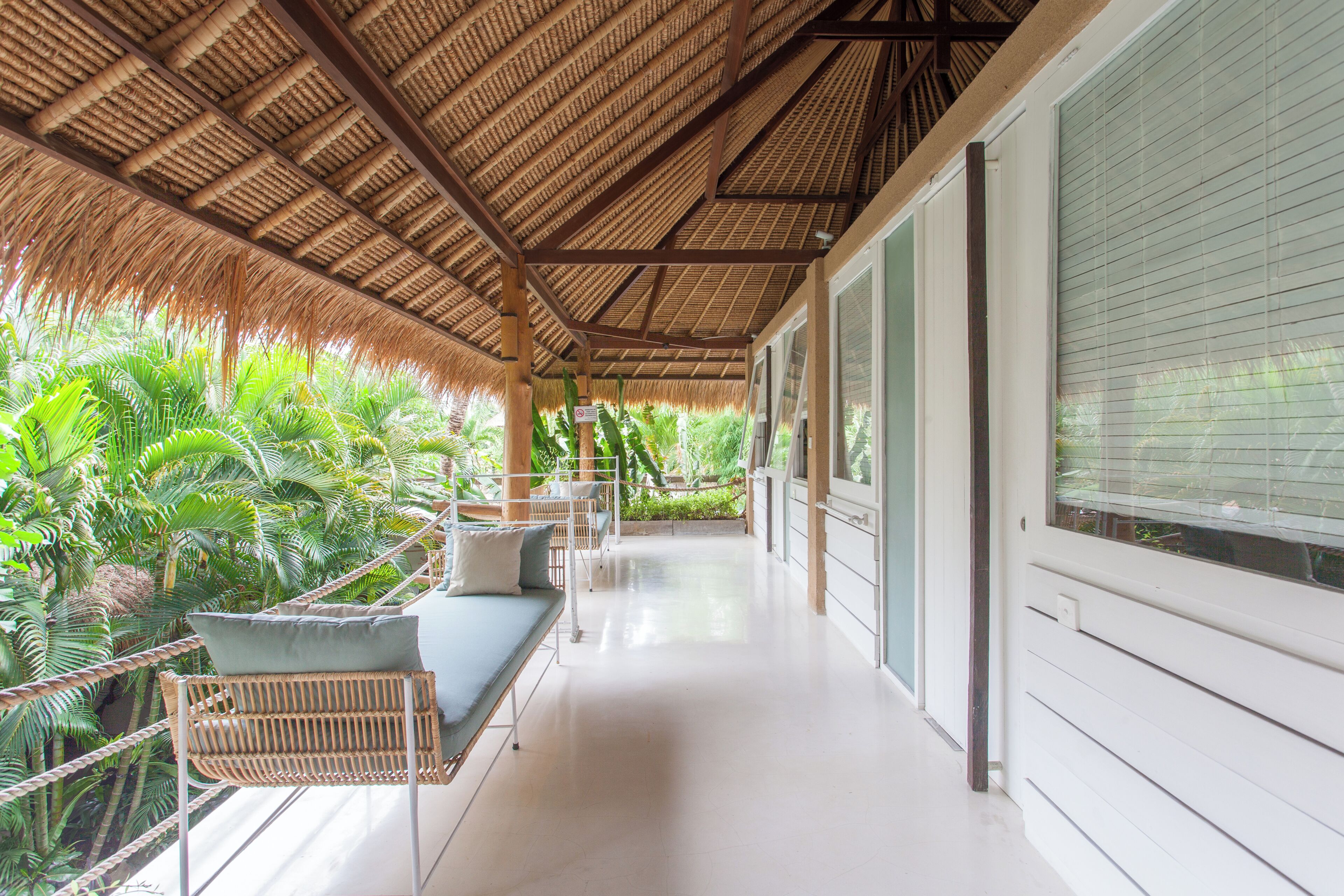 A covered balcony with a thatched roof, seating area, and lush tropical plants.