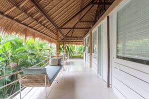A covered balcony with a thatched roof, a white sofa, and lush green plants.