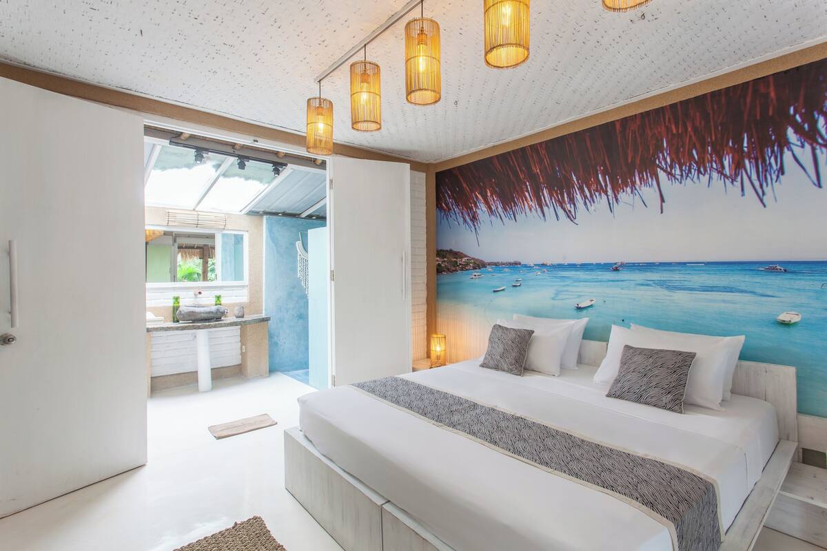 Un dormitorio con una cama grande, un cuadro de una playa y vista al mar.