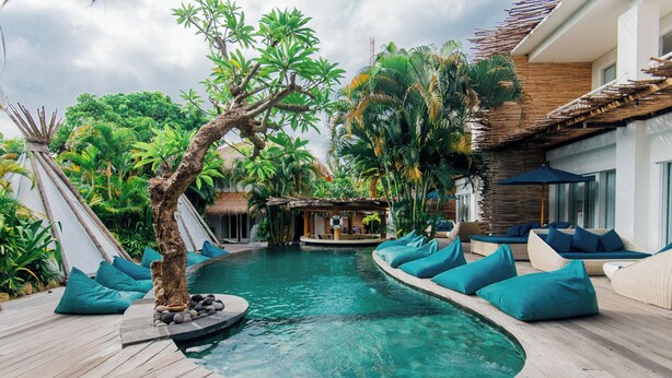 A pool area with a wooden deck, a small waterfall feature, and lounge seating with teal cushions. - Kima Surf Camp Bali Seminyak (Seminyak)