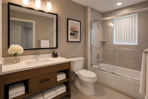 A modern bathroom with a large mirror, a toilet, a shower, and a vanity with a sink and towel storage. - The Montclair Suites (Toronto)