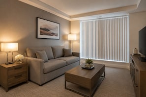 A modern living room with a sofa, a coffee table, a TV, and a window with blinds. - The Montclair Suites (Toronto)