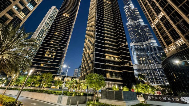 A nighttime view of high-rise buildings with modern architecture, including a prominent skyscraper with a spire. - Address Opera 1BR, Boulevard View-Hotel Style Stay (Dubai)