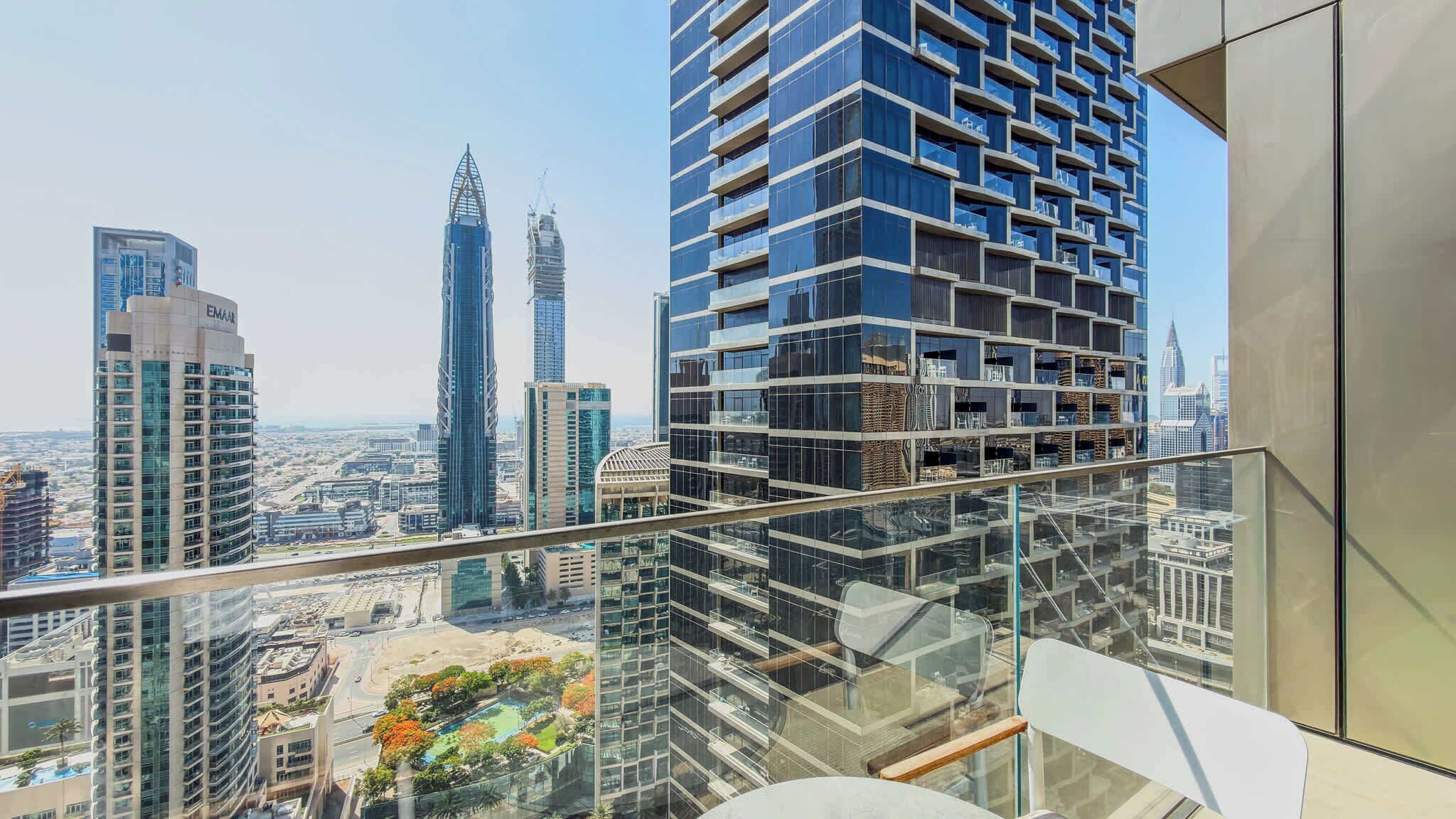 A high-rise building with a modern glass facade, a view of the cityscape, and a balcony with a glass railing.