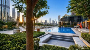 A rooftop pool with lounge chairs, a tree, and a city skyline in the background. - Address Opera 1BR, Boulevard View-Hotel Style Stay (Dubai)