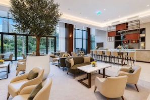 Eine moderne Hotellobby mit einem großen Baum, Sitzbereichen, einer Bar und einer Küche im Hintergrund.