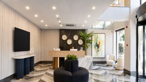 Un área de recepción moderna con suelo de mármol, un mostrador de recepción, un reloj grande y una planta en maceta.