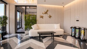 Un vestíbulo moderno con un sofá blanco, un banco negro, una planta en maceta y contenedores de reciclaje.