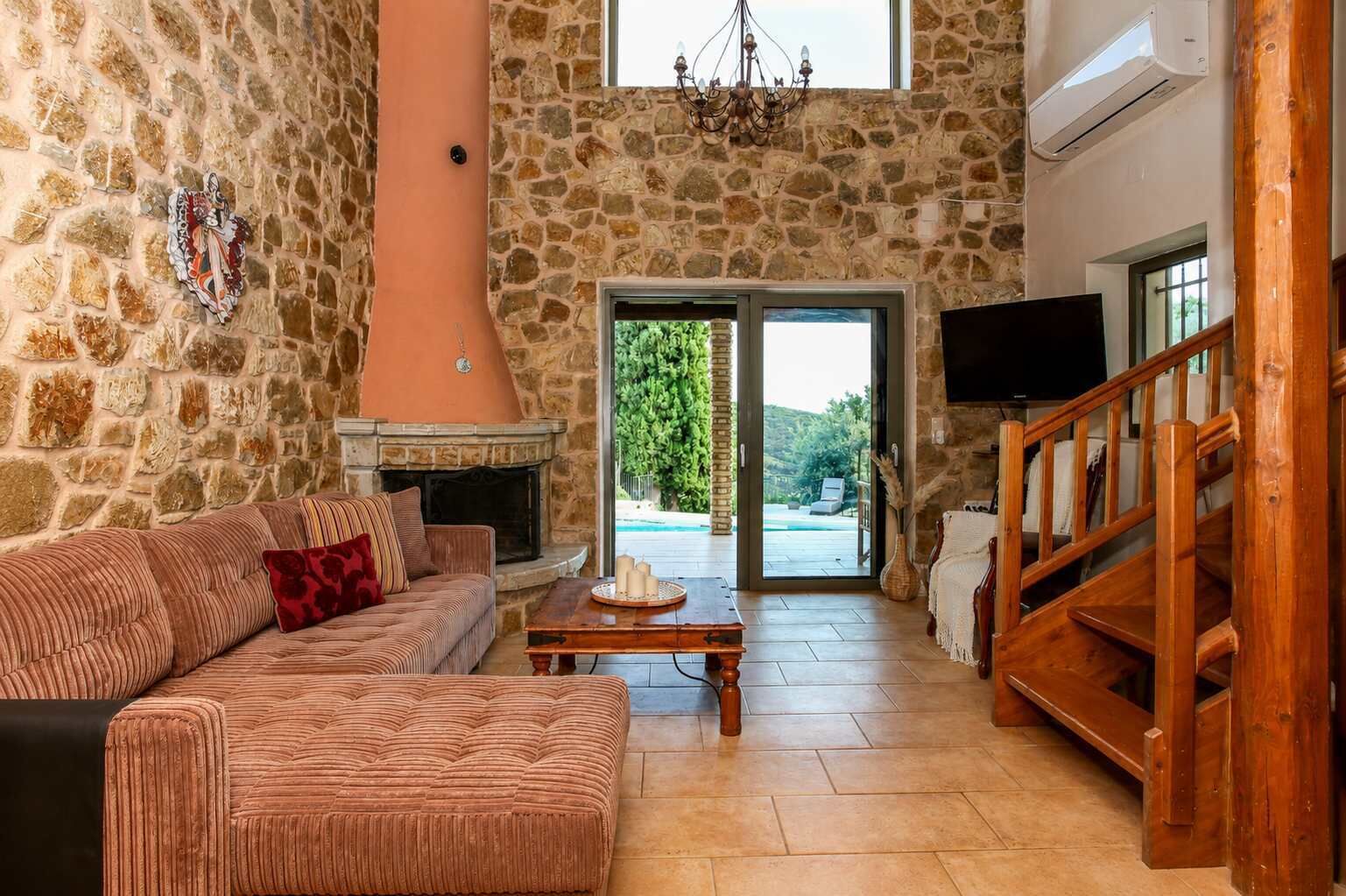 A stone-walled room with a fireplace, a sofa, a wooden table, and a TV.