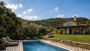 A stone house with a pool, surrounded by a well-maintained lawn and trees.