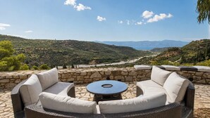 A patio with wicker furniture and a stone table, overlooking a mountainous landscape.