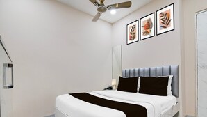 Een moderne slaapkamer met een bed, een plafondventilator, een nachtkastje met een lamp en twee kunstwerken in lijsten aan de muur.
