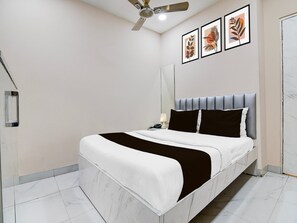 A modern bedroom with a bed, a ceiling fan, a bedside table with a lamp, and two framed artworks on the wall. - Super Marquis Street Formerly BK International (Kolkata)
