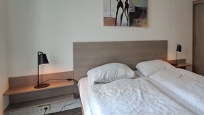 A bedroom with a bed, two bedside lamps, a painting on the wall, and a wooden nightstand. - Holiday Home in Brunssum With Terrace (Brunssum)