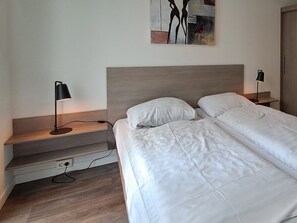 Ein Schlafzimmer mit einem Bett, zwei Nachttischlampen, einem Bild an der Wand und einem Holznachttisch.